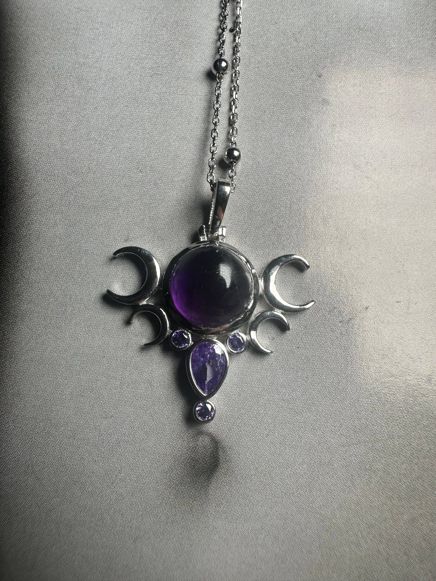 Silver pendant with purple gemstones on a chain against a gray background