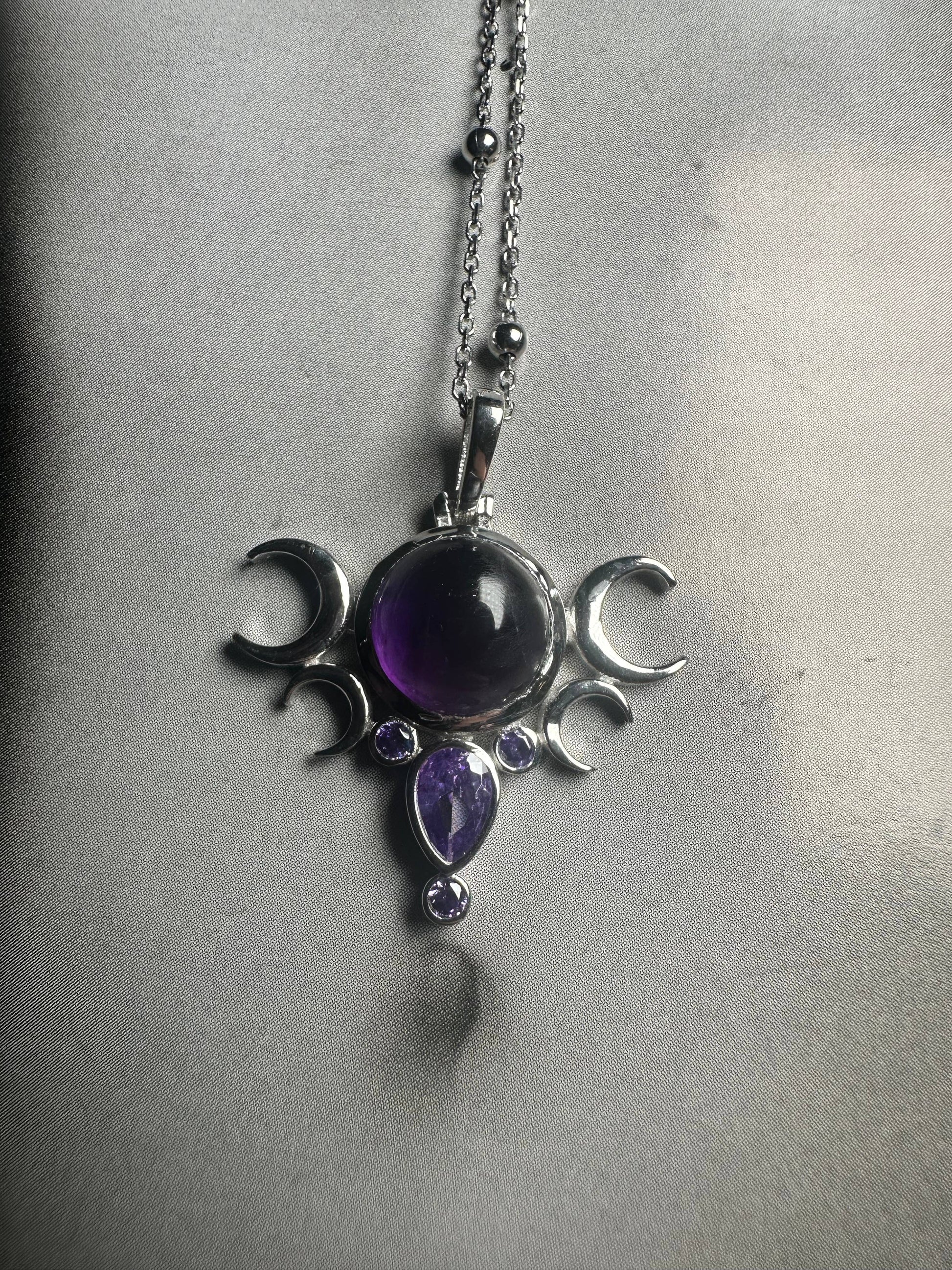 Silver pendant with purple gemstones on a chain against a gray background