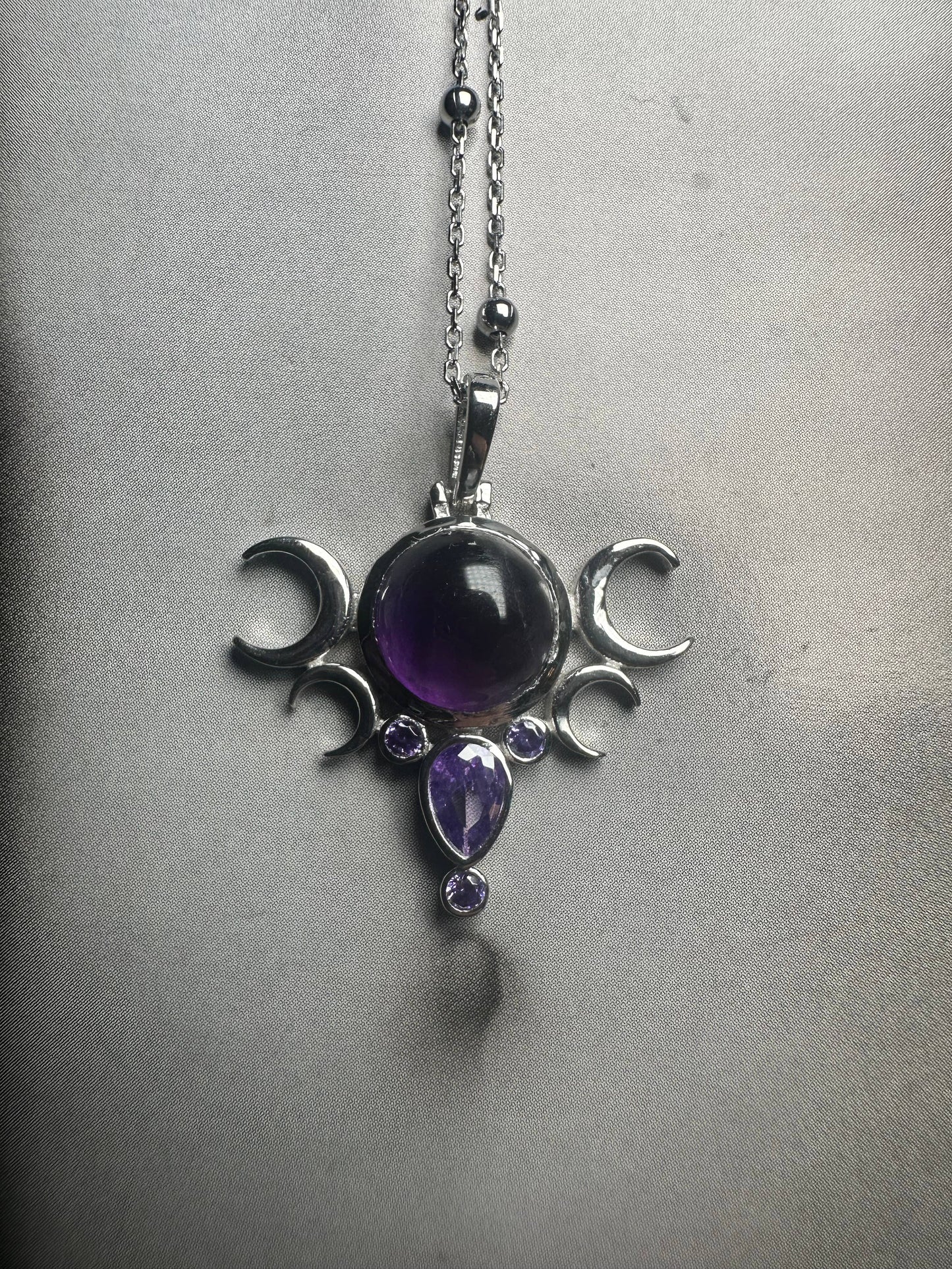 Silver pendant with purple gemstones on a chain against a gray background