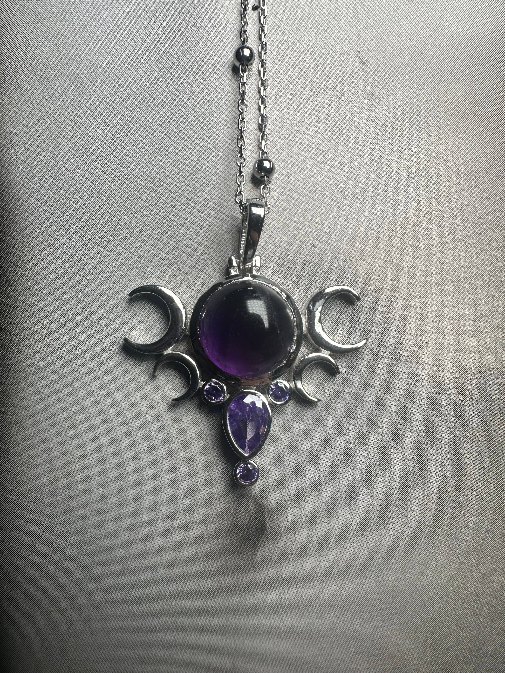 Silver pendant with purple gemstones on a chain against a gray background