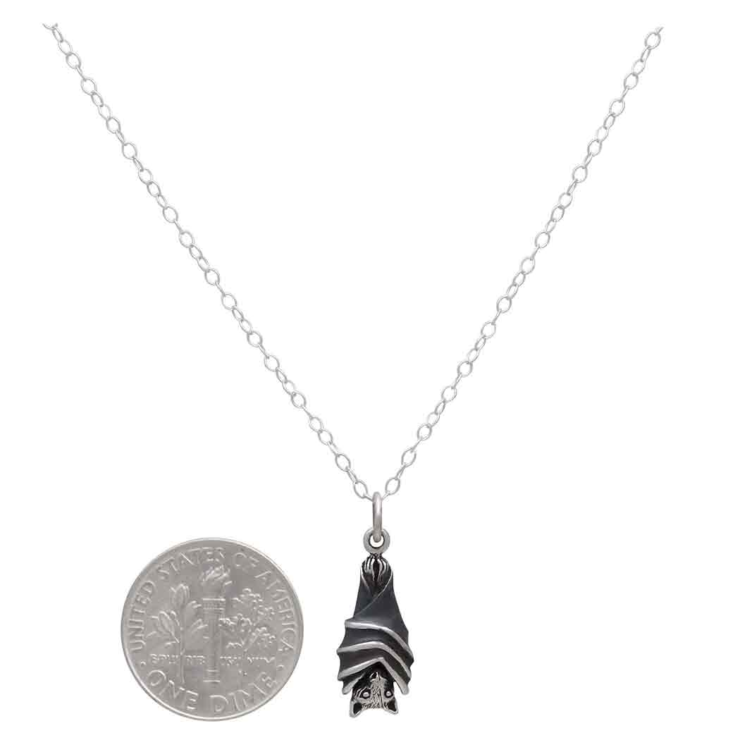 Silver necklace with a hanging bat pendant on a white background next to a dime for scale- Shadowplay Collection Gift Shop