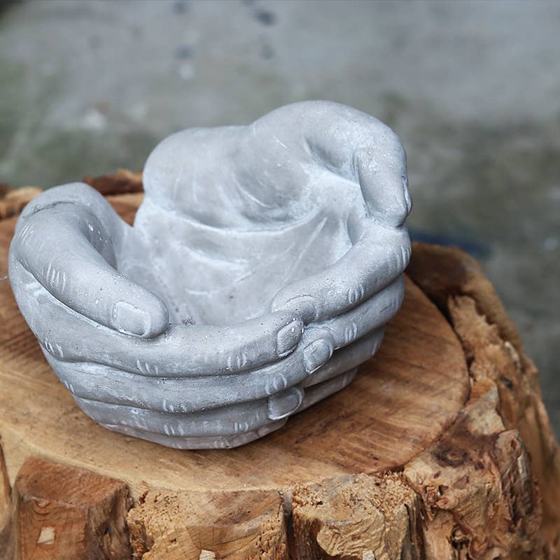 Gray stone sculpture of hands holding a heart on a wooden stump