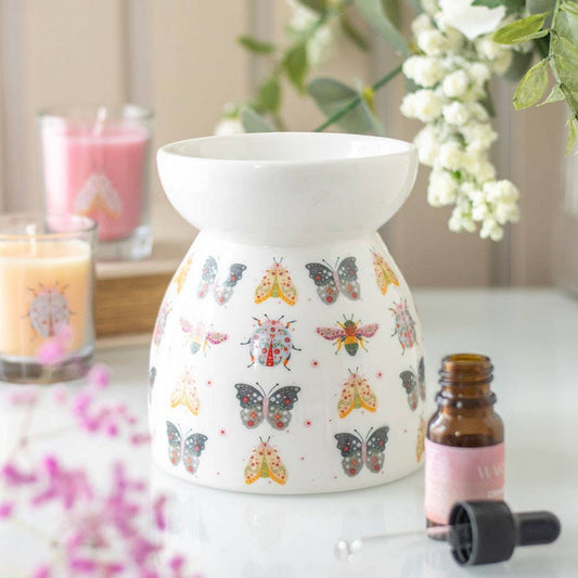 Ceramic Oil Warmer with floral bug  designs on a table with candles and flowers.- Shadowplay Collection Gift Shop