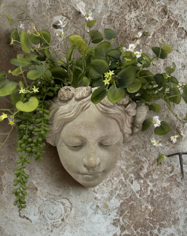 Decorative wall piece with a face sculpture and greenery on a textured wall.- Shadowplay Collection Gift Shop