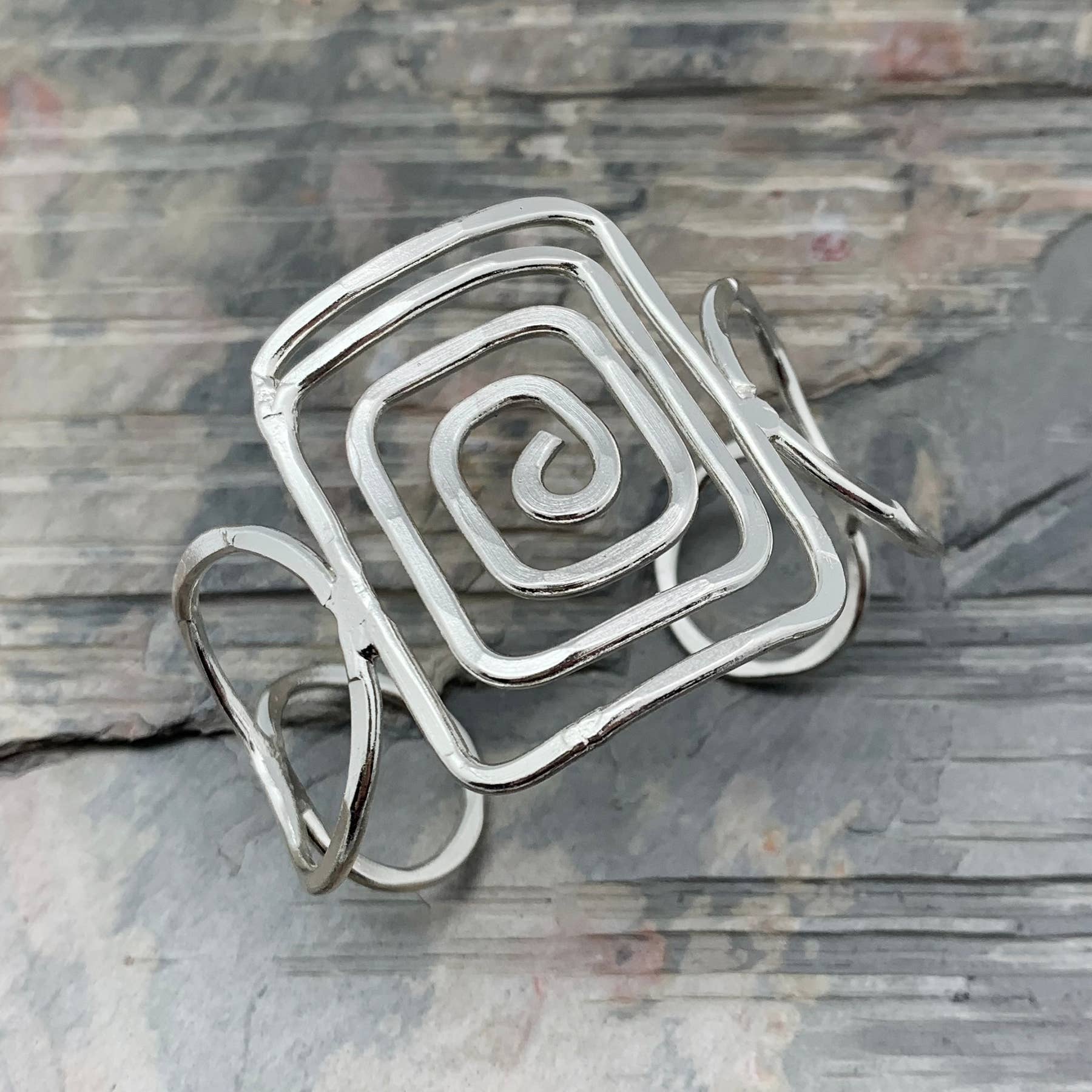 Silver spiral bracelet on a textured stone surface- Shadowplay Collection Gift Shop