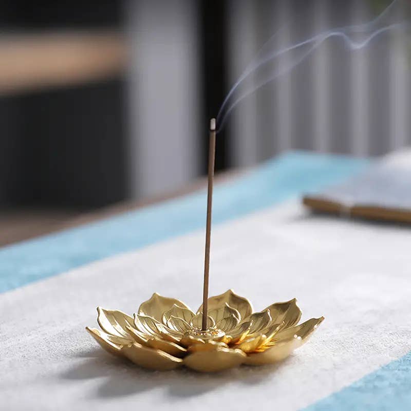 Gold lotus-shaped incense burner with a smoking incense stick on a blurred background- Shadowplay Collection Gift Shop