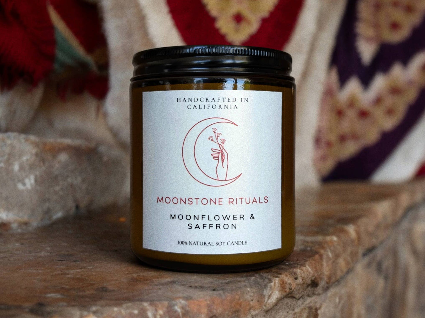 Candle jar labeled 'Moonstone Rituals' with 'Moonflower & Saffron' on a stone surface.