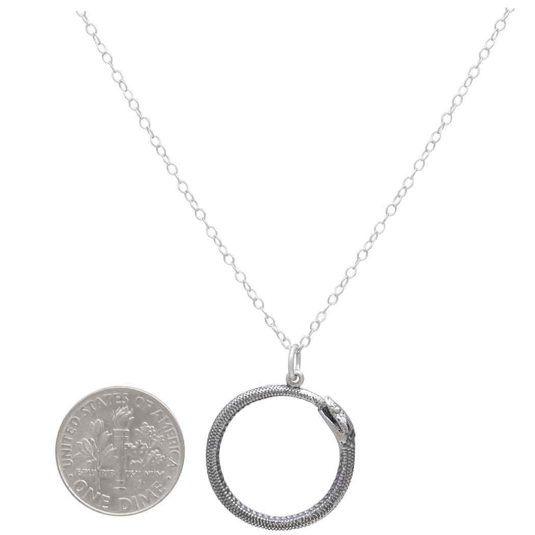 Silver circular pendant necklace with a coin for scale on a white background