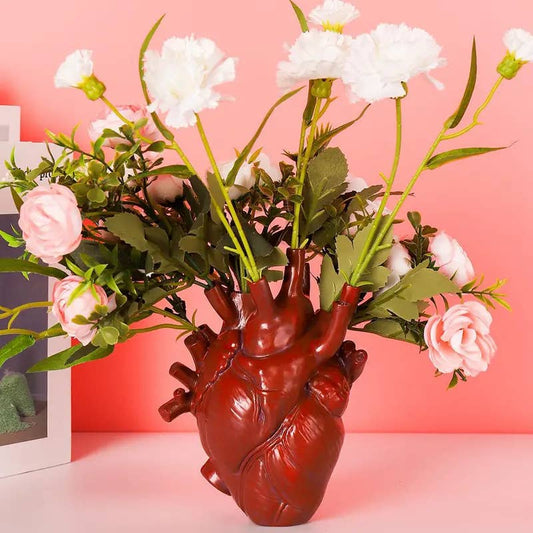 Red Heart-shaped vase with flowers against a pink background