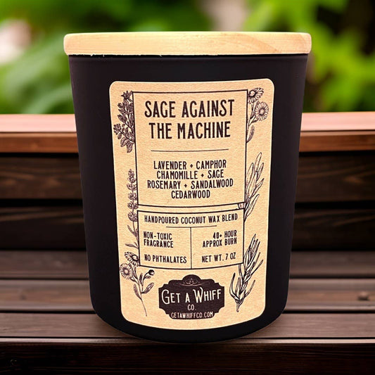 Picture of Sage Against the Machine Candle on wood ledge with greenery in the background- Shadowplay Collection Gift Shop