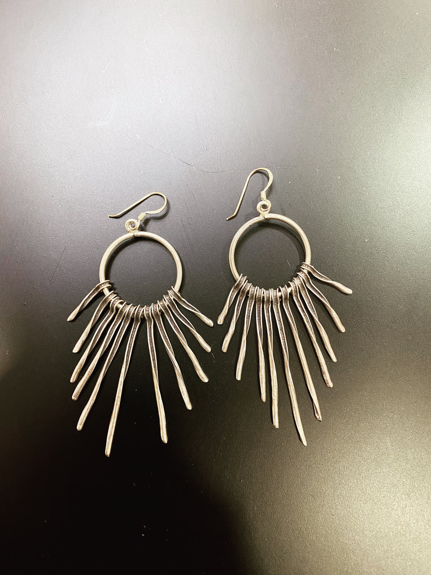 Pair of silver hoop earrings with dangling bars on a dark background