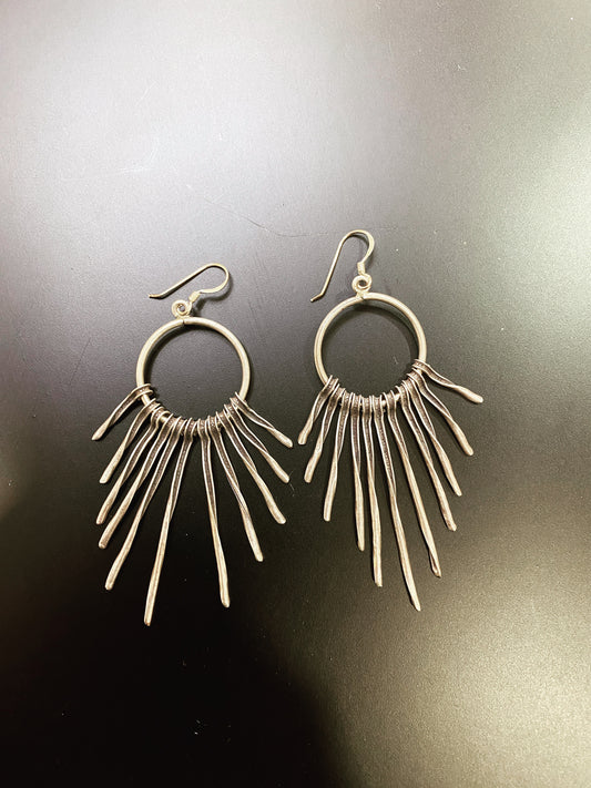 Pair of silver hoop earrings with dangling bars on a dark background