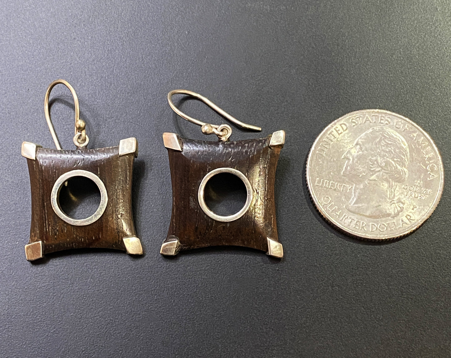 Pair of square earrings with gold accents on a dark surface next to a coin for scale.