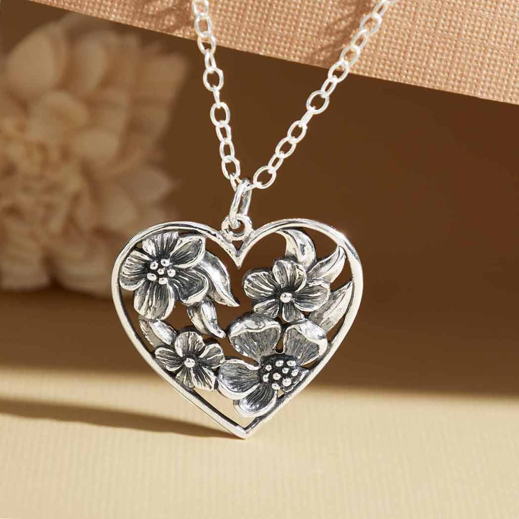 Silver heart-shaped necklace with floral designs on a beige background- Shadowplay Collection Gift Shop in San Antonio, TX