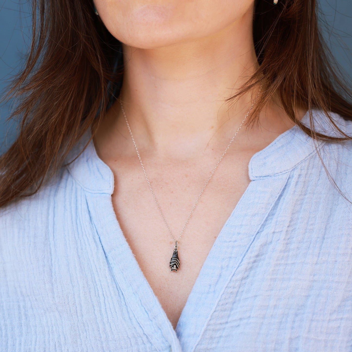 Sterling Silver Bat Necklace with a pendant worn by a person in a light blue shirt against a neutral background- Shadowplay Collection