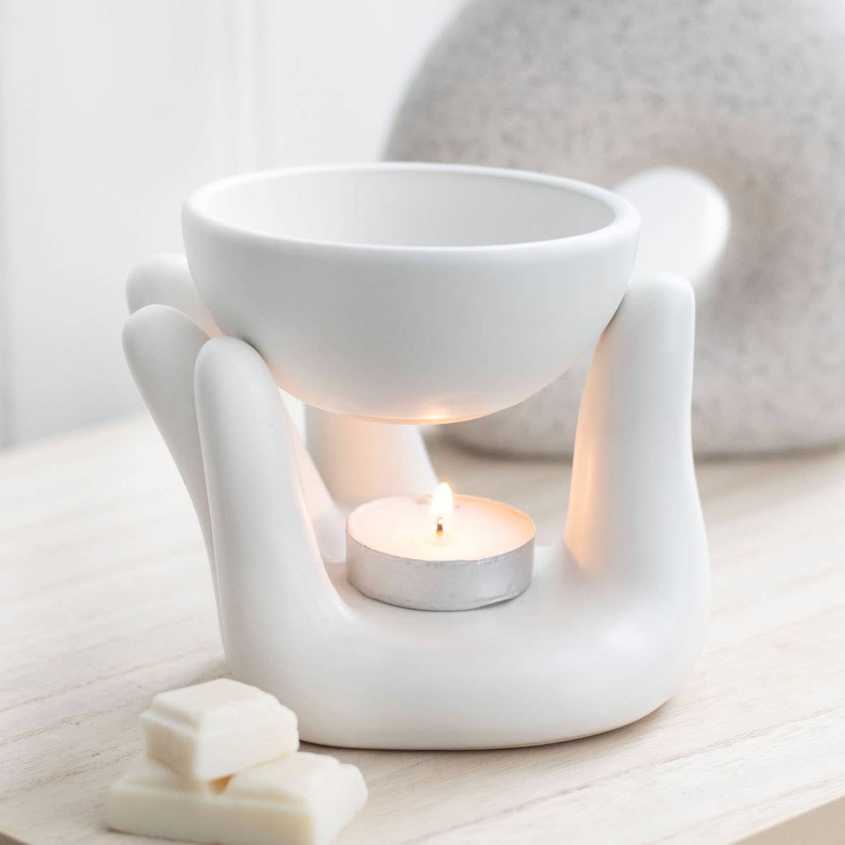 White ceramic wax warmer with a lit tealight candle on a light wooden surface.- Shadowplay Collection Gift Shop
