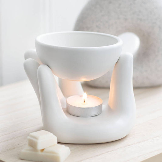 White ceramic wax warmer with a lit tealight candle on a light wooden surface.- Shadowplay Collection Gift Shop