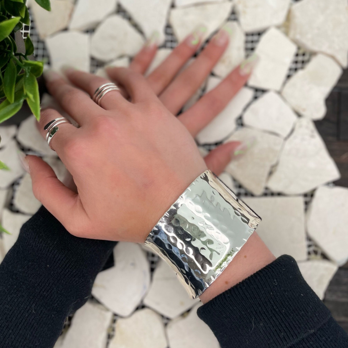 Hand wearing a silver bracelet and rings on a mosaic tile background
