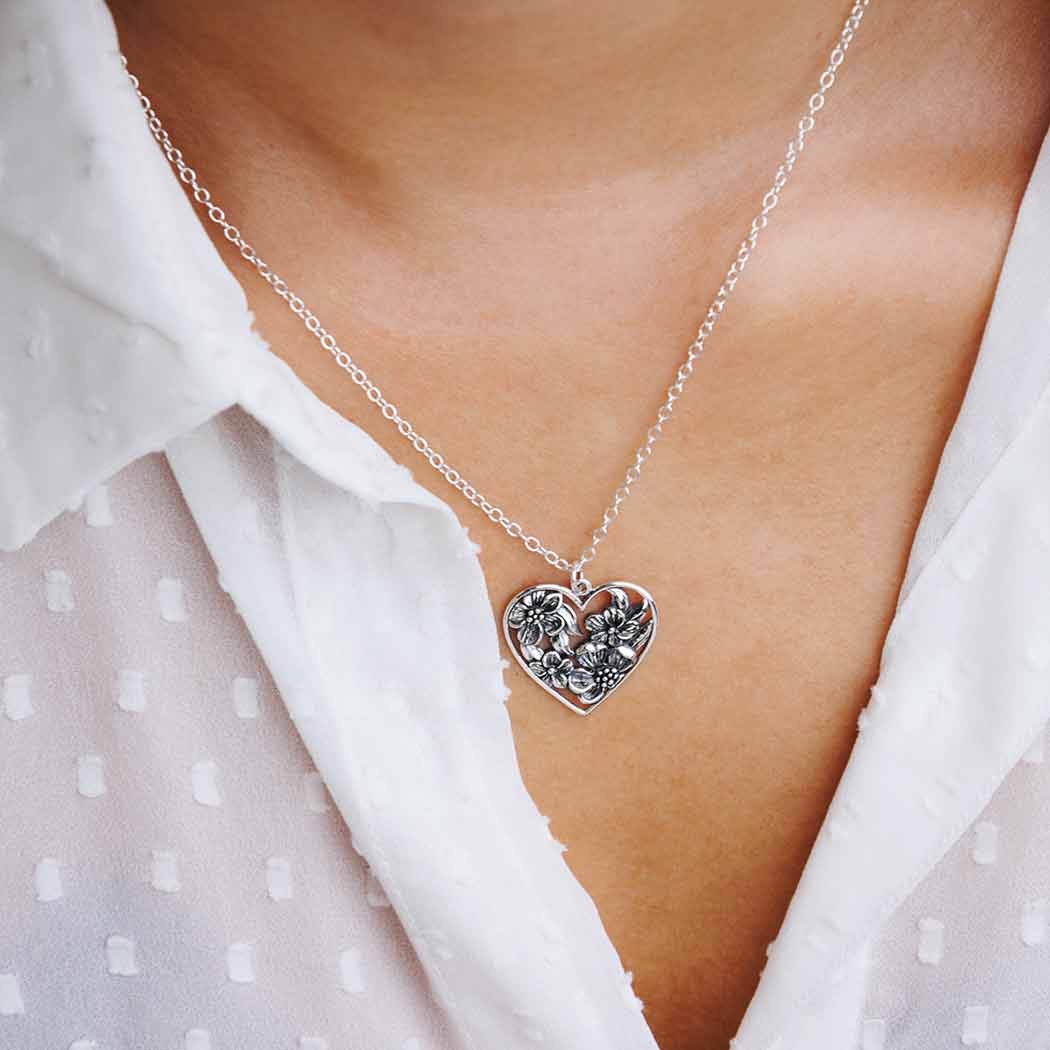 Silver heart-shaped necklace with floral design worn by a person in a white blouse.- Shadowplay Collection Gift Shop