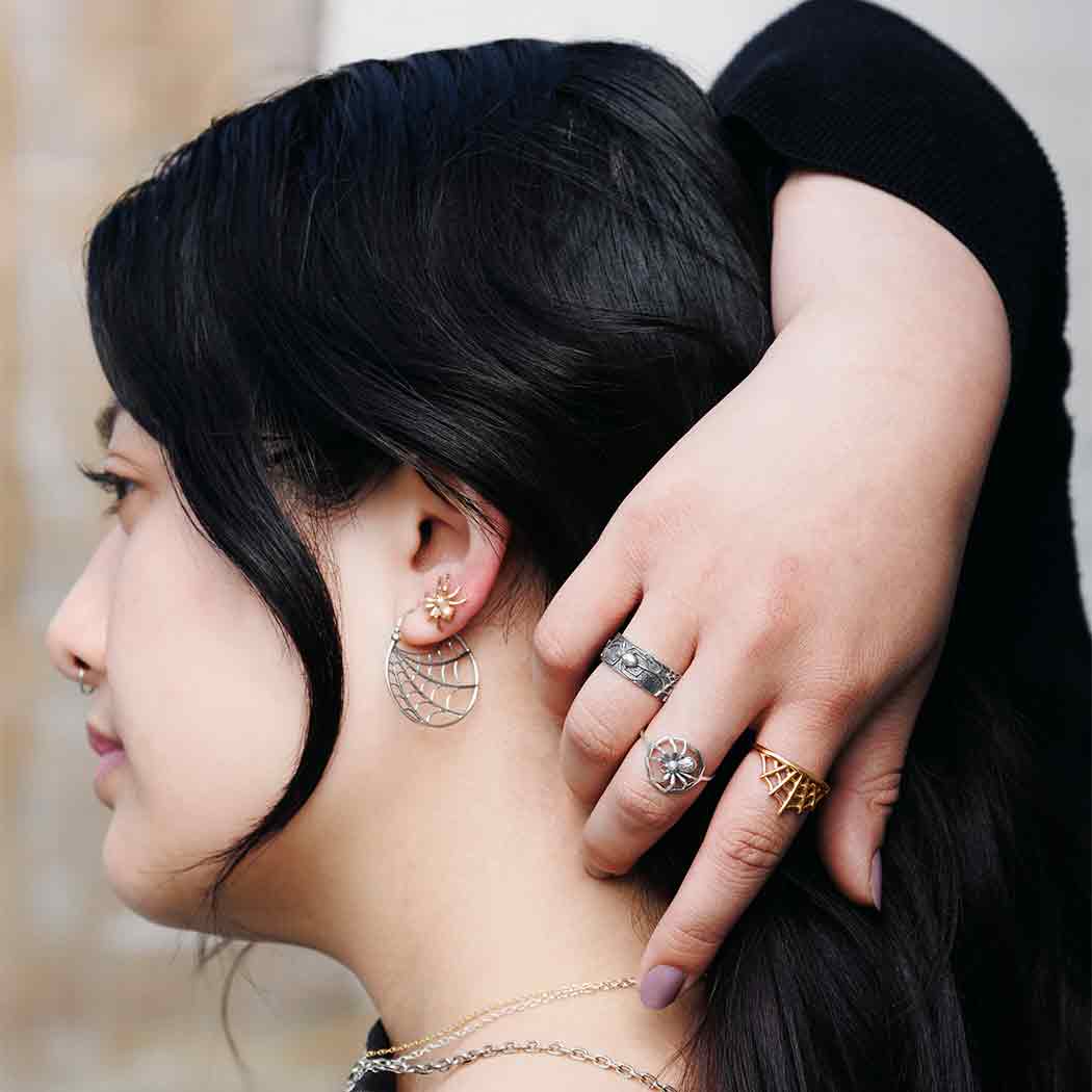 Close-up of a person wearing multiple rings and spiderweb earrings with a blurred background- Shadowplay Collection Gift Shop