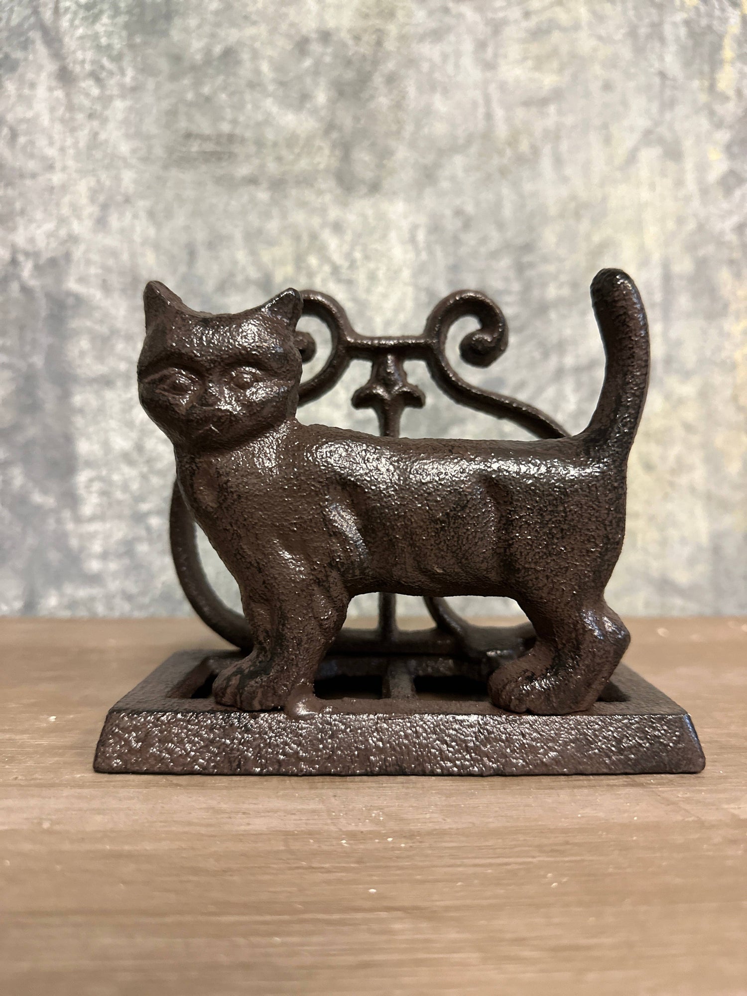 Cast iron cat-shaped napkin holder on a wooden surface with a textured gray background- Shadowplay Collection Gift Shop